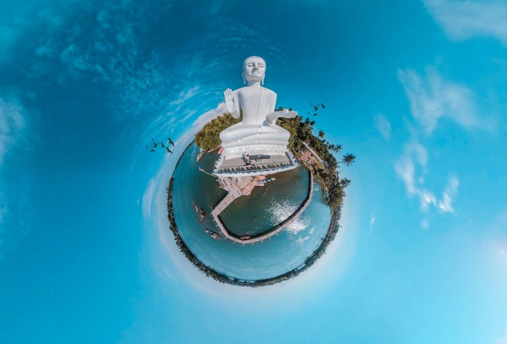Tiny planet view of a Buddha statue surrounded by water and palm trees in Sri Lanka.